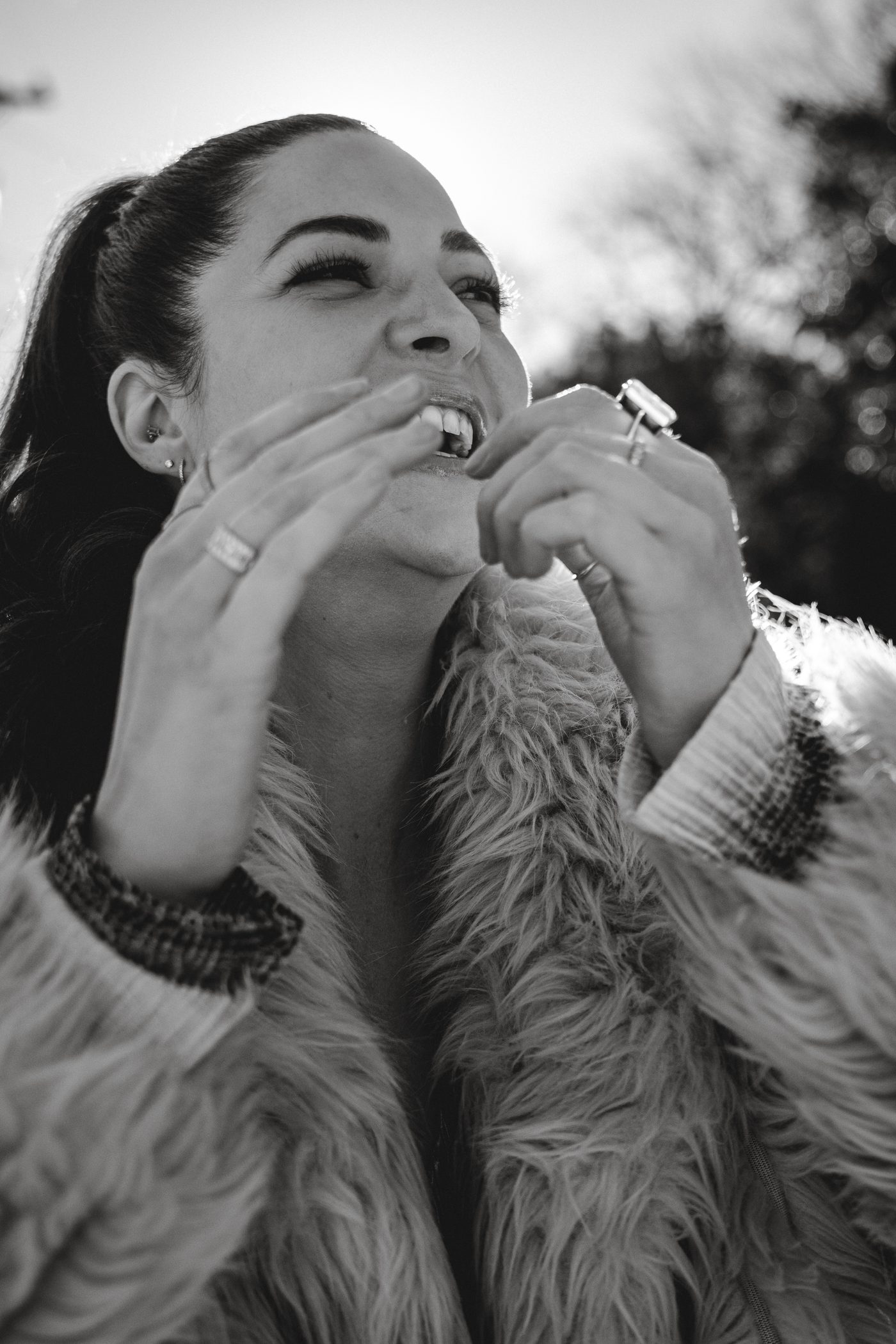 Ellie Rivers laughing outdoors in a faux-fur coat, black-and-white portrait